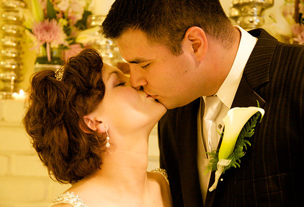 A man and woman kissing in front of flowers.